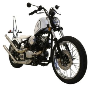 A motorcycle is parked on the ground in front of a white wall.